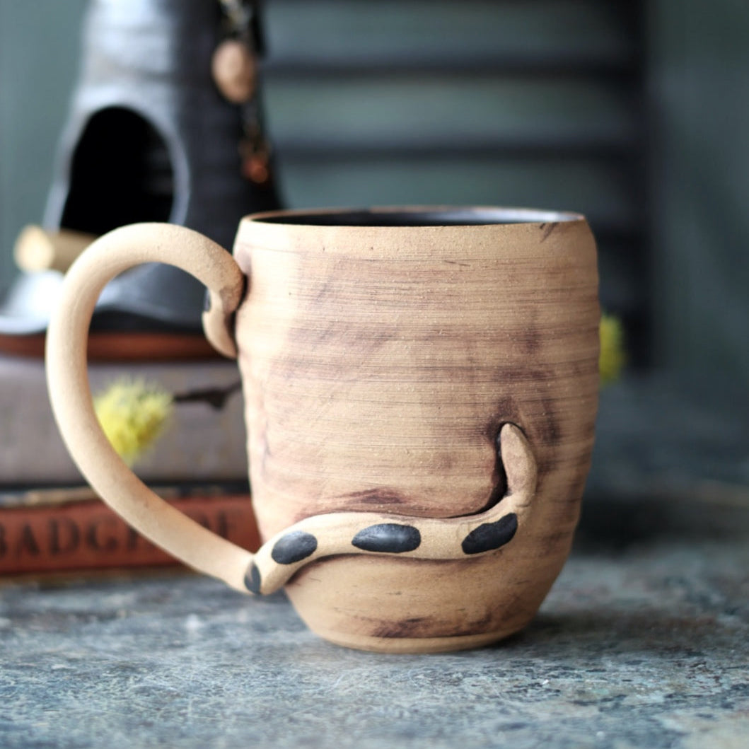 Handmade pottery mug with a snake design on a textured surface