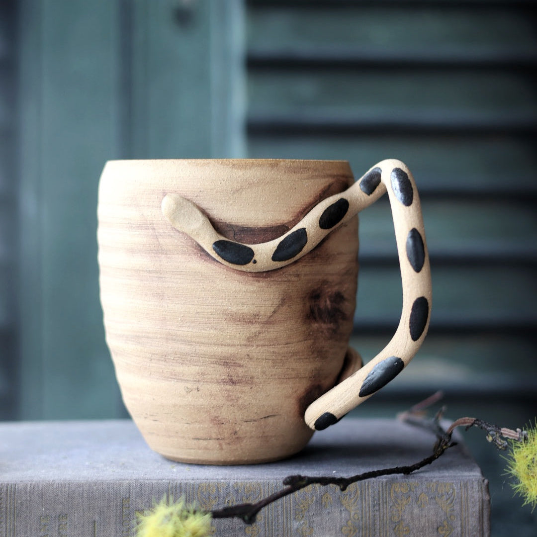 Handmade pottery mug with a black spotted snake handle on top of books