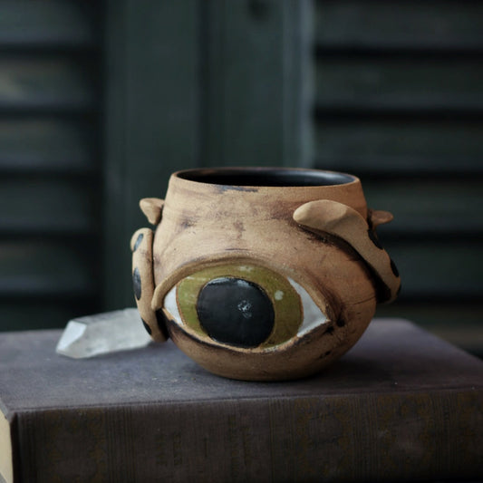 Ceramic pot with eye design on a dark surface